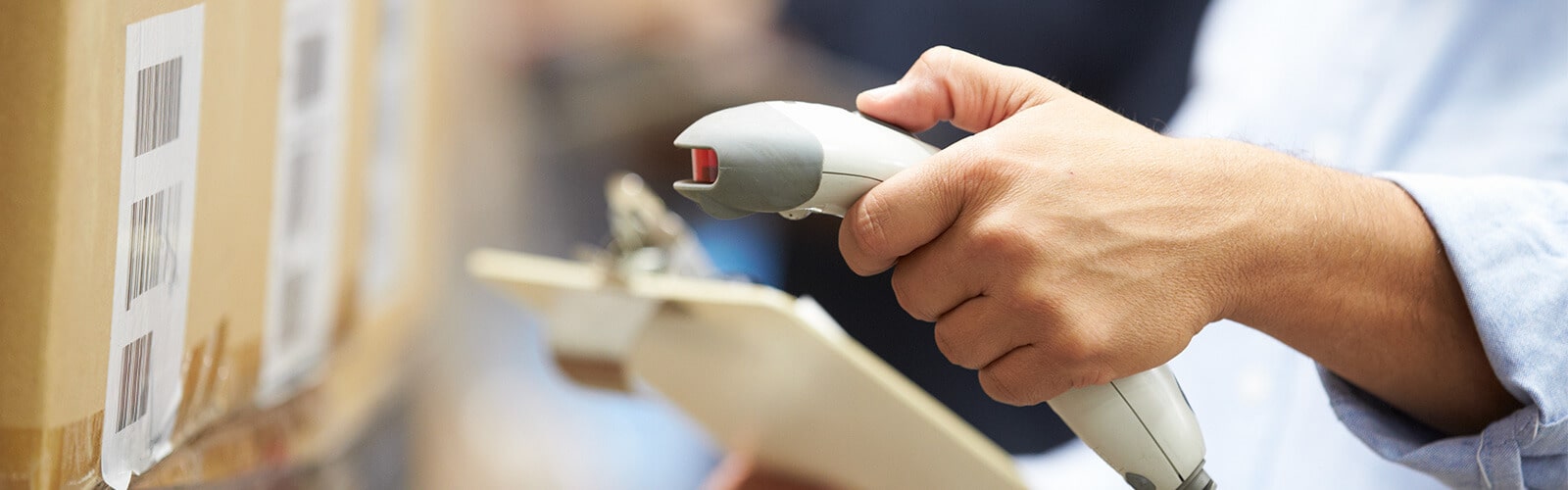 Warehouse worker with a clipboard scanning a box with a handheld scanner.