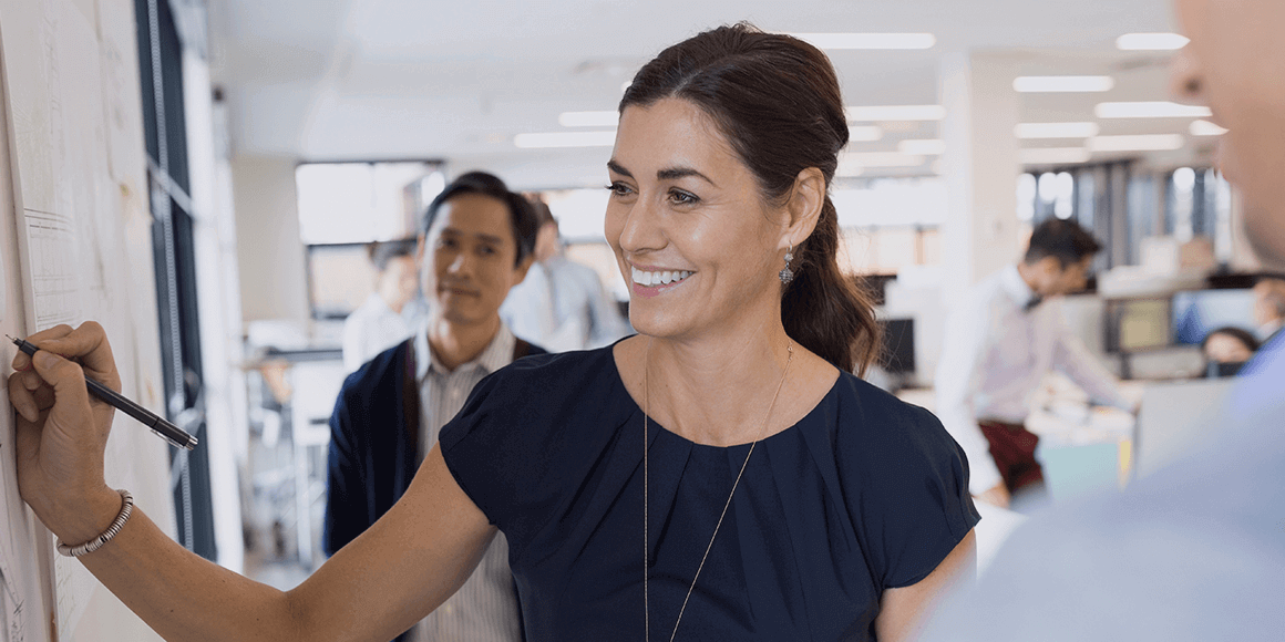 Female professional leading a team discussion and taking notes on a board.