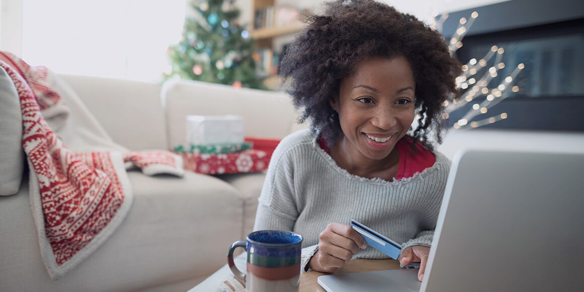 A woman sitting in her Christmas decorated living room making a purchase on her laptop.