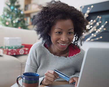 A woman sitting in her Christmas decorated living room making a purchase on her laptop.