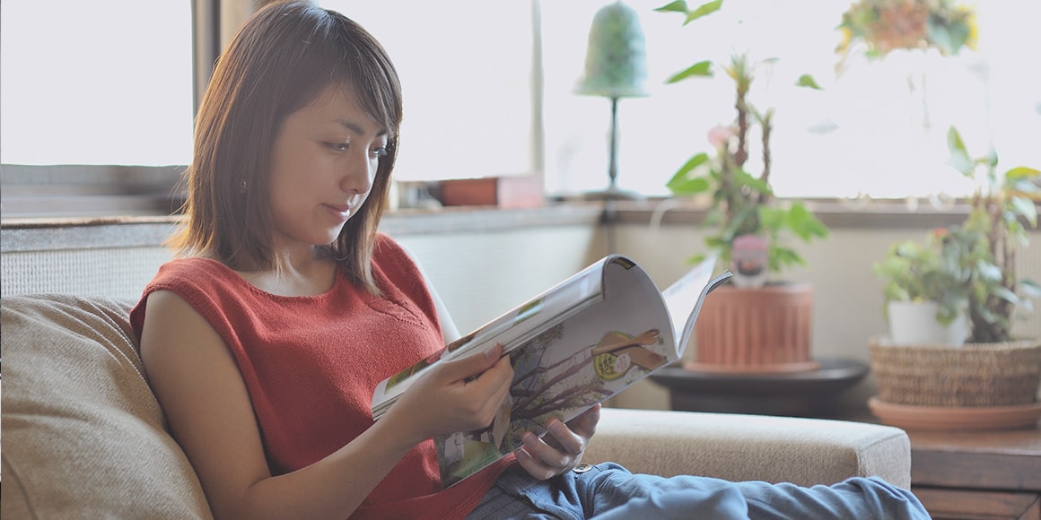 A woman relaxing on a couch and reading a magazine.