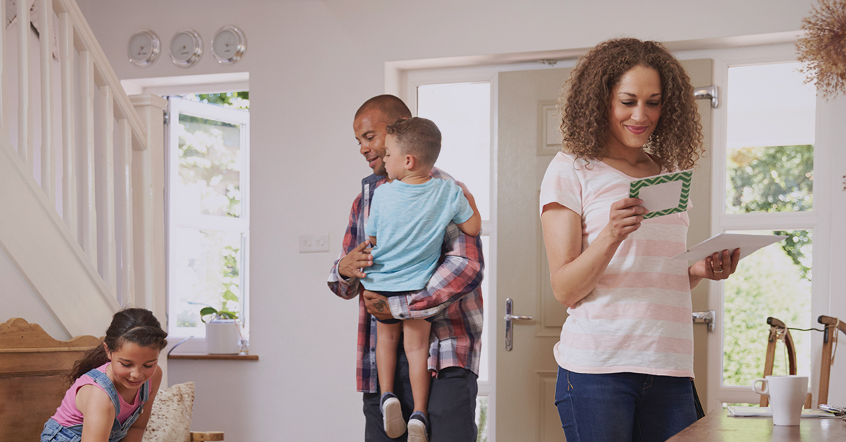 A woman is reading a card she received in the mail with her family beside her.