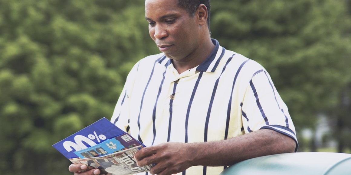 A male leaning against a subject and reading over a coupon.