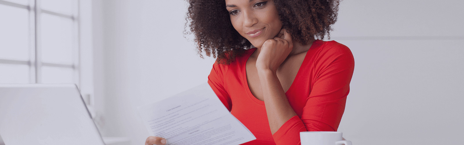 A woman reading a paper document over her computer.