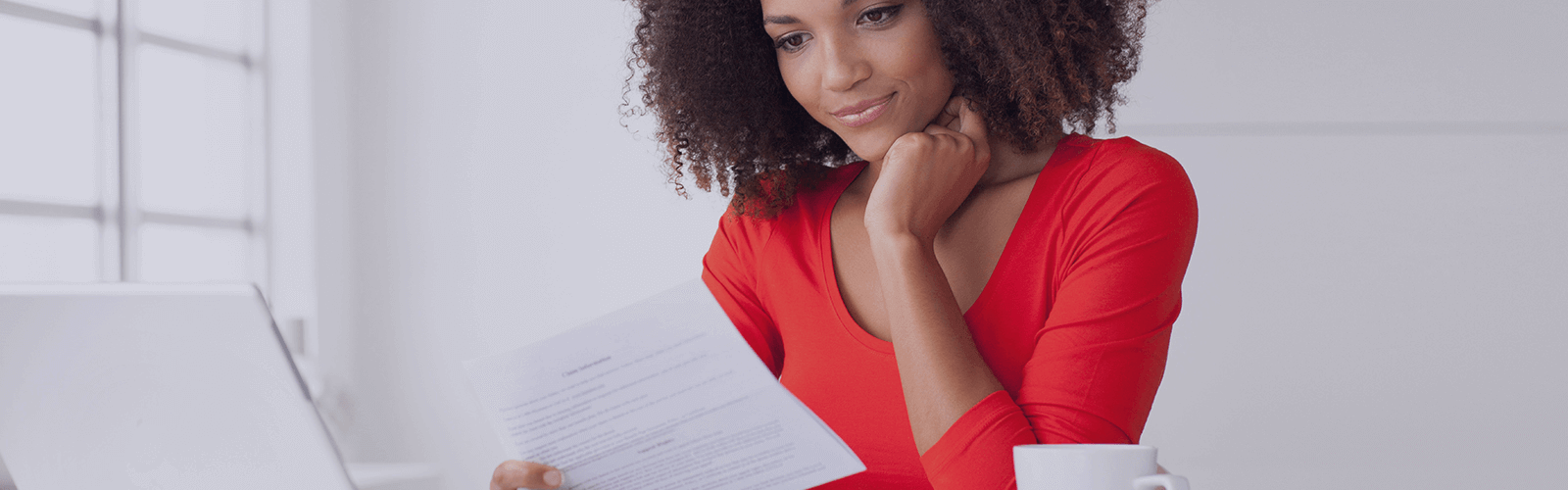 A woman reading a paper document over her computer.