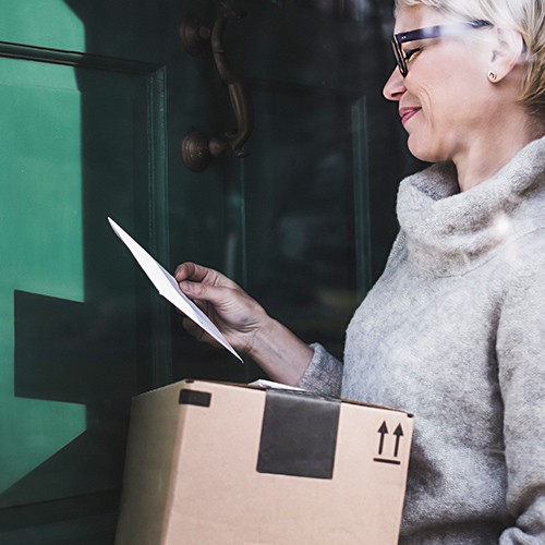 A woman looking at mail and a package she's received at home and smiling.