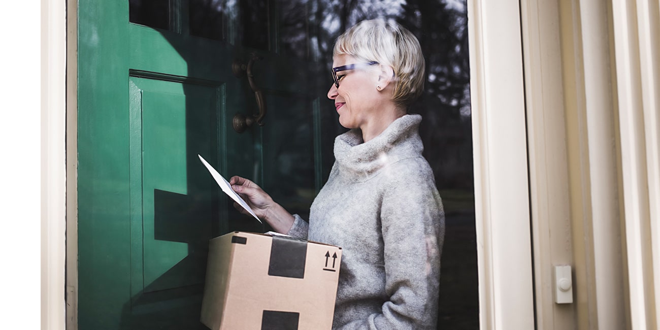 A woman looking at mail and a package she's received at home and smiling.