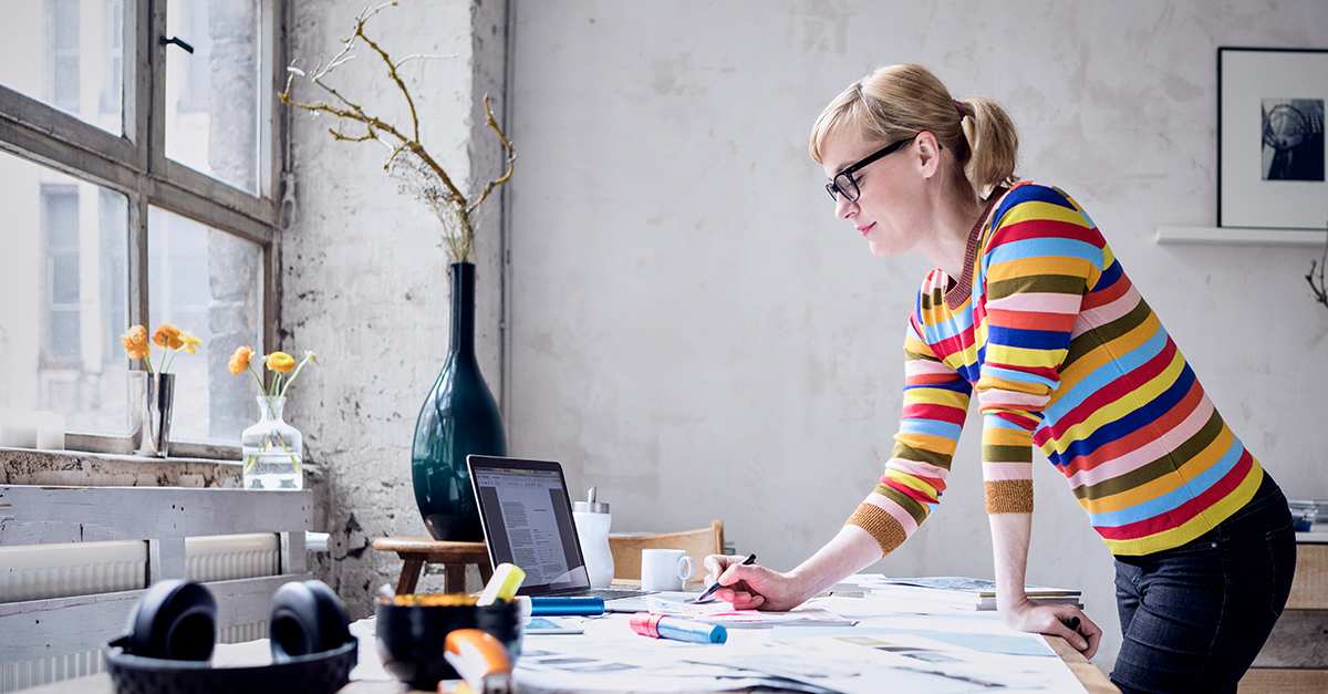 A professional looking at a laptop and writing at her desk.