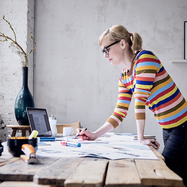 A professional looking at a laptop and writing at her desk.