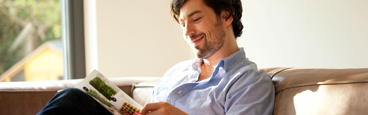 A man relaxing on a leather couch reading magazine.