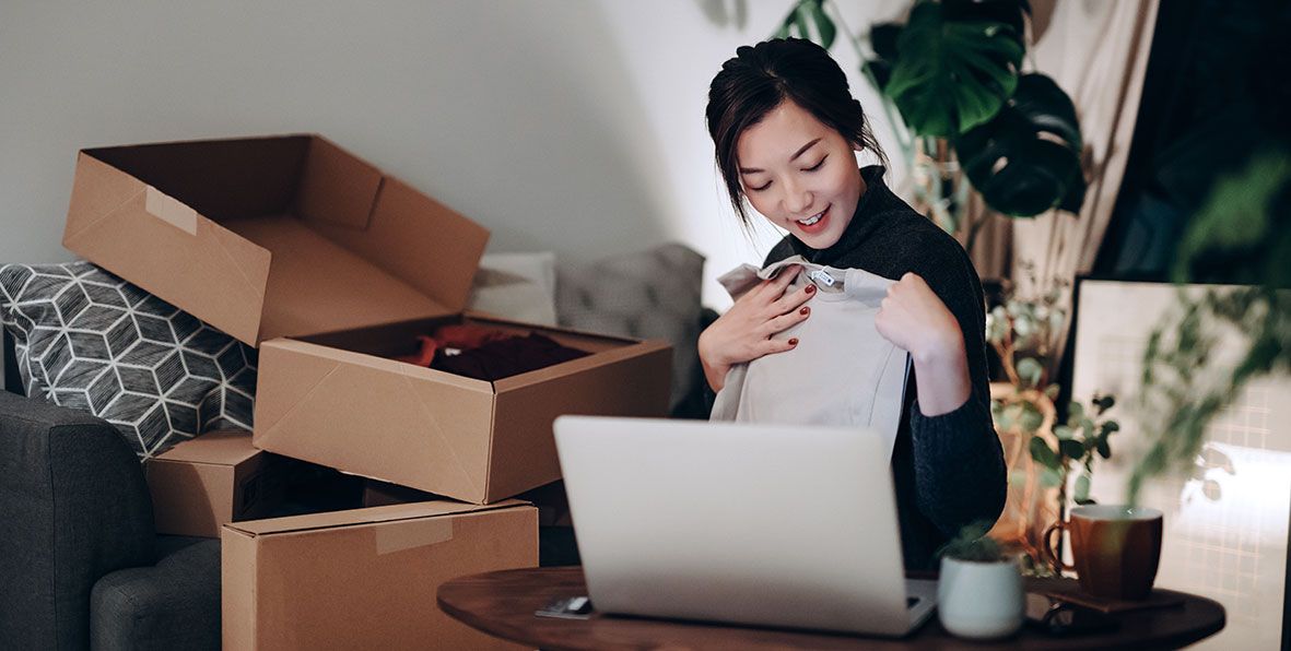 A young woman smiling while opening packages and looking at her laptop.