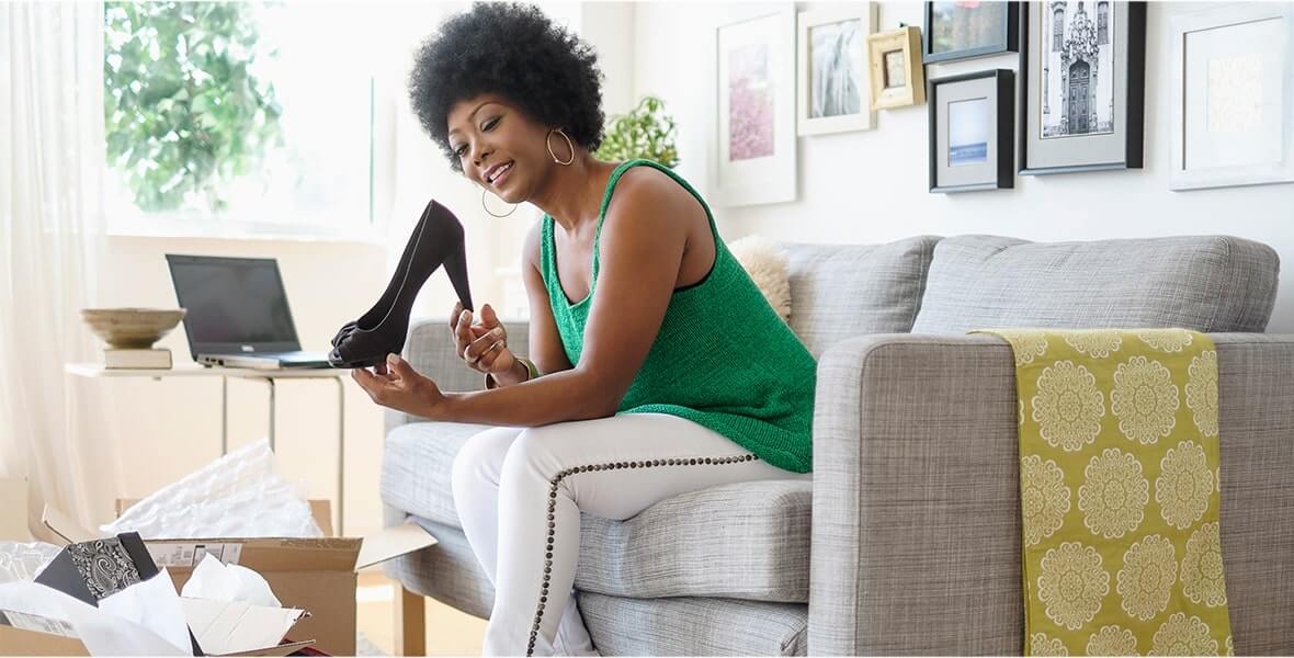 A woman sitting on her couch, looking at black high-heel shoes she received in the mail.