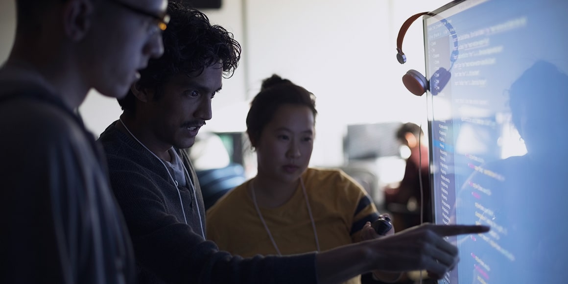 Three coworkers analyzing data on a digital board.