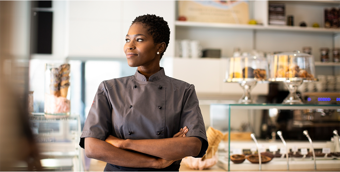 A female pastry chef in a gray chef uniform standing in front of the bakery counter.