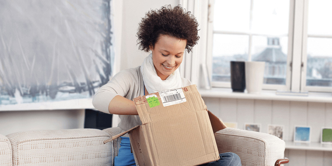 A happy customer is opening a USPS package on the sofa