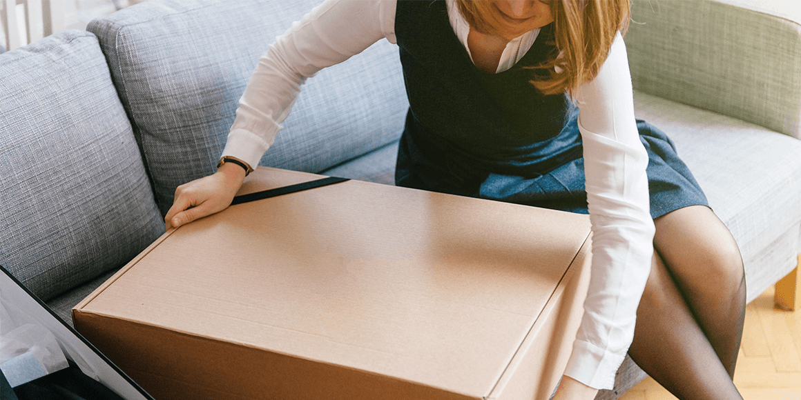 A woman sitting beside a large box on a couch.