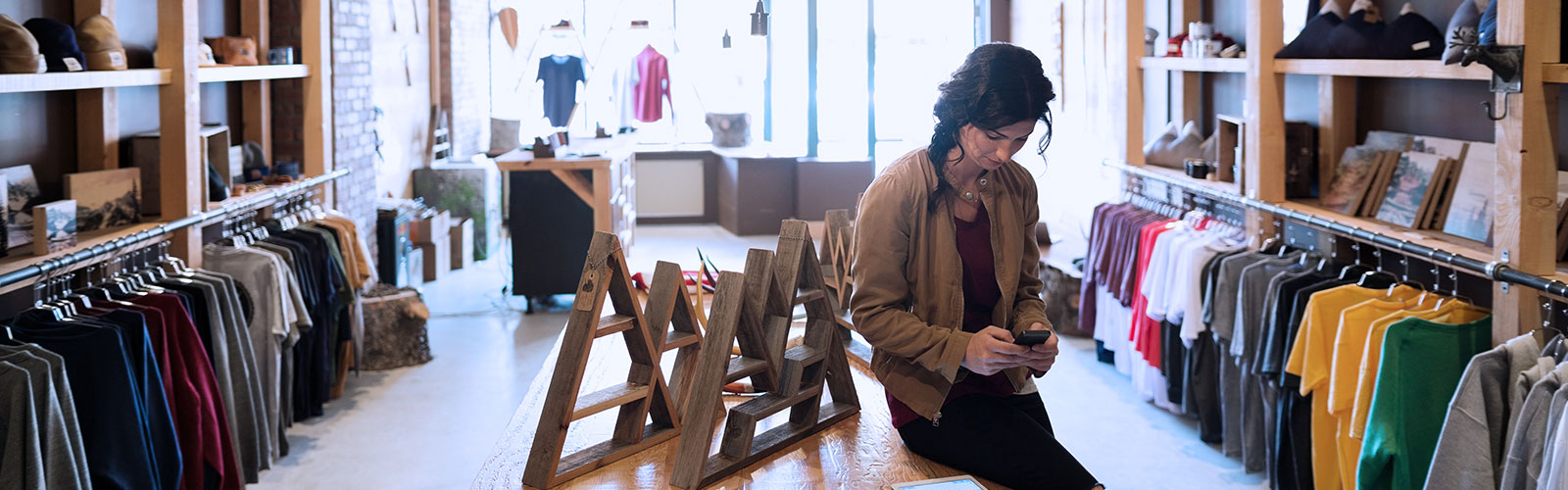 A woman sitting on a wooden table in a clothes shop.