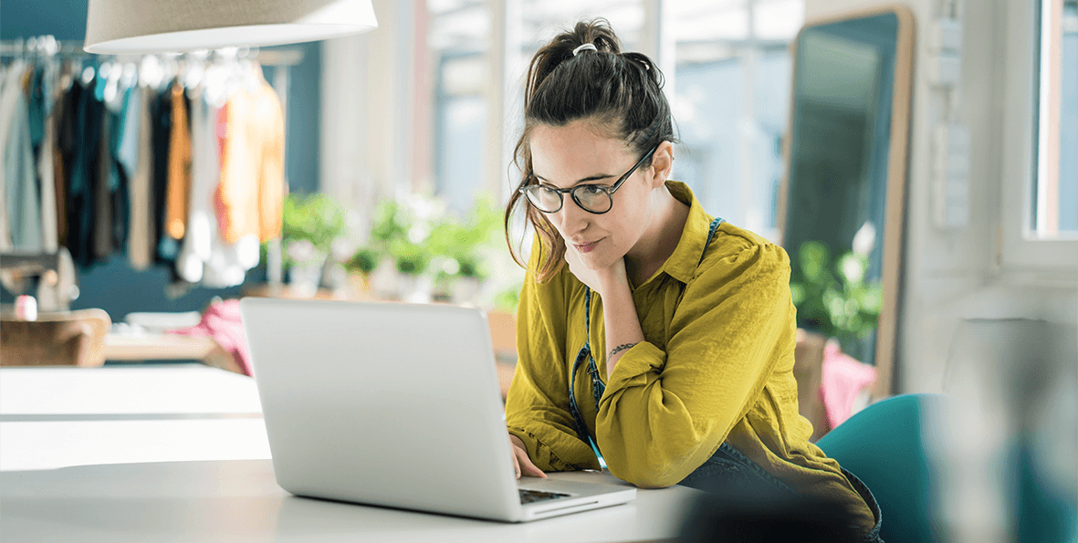 A woman dressed in a yellow blouse leaning into her computer work at the office.