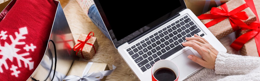 Someone on the floor with a cup of coffee, their computer, and holiday gifts.