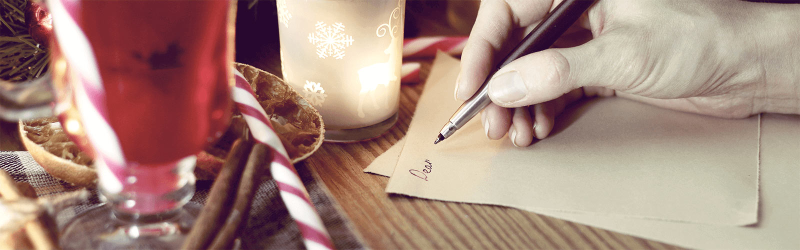 Someone writing a letter beside holiday decorations, including a candy cane and a candle.