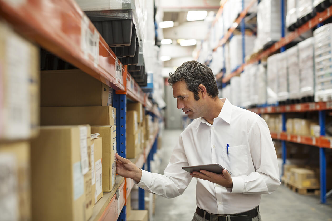 A professional in a white shirt holding a tablet and checking a package in a warehouse.