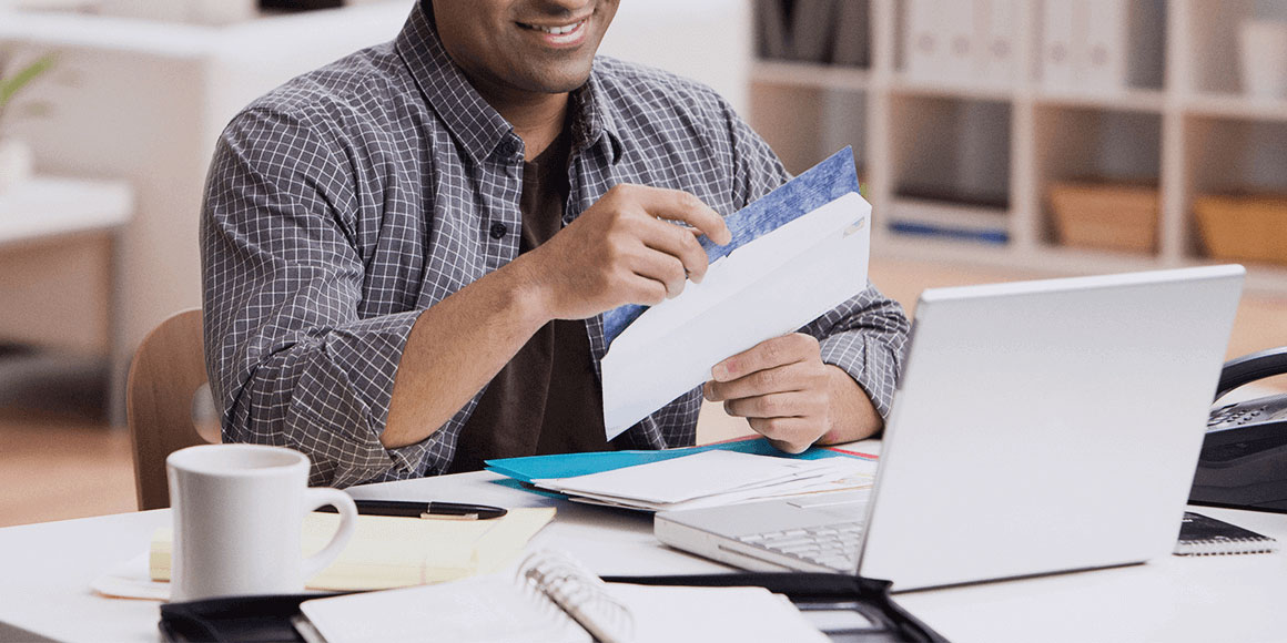 A man opening his mail beside his office computer.