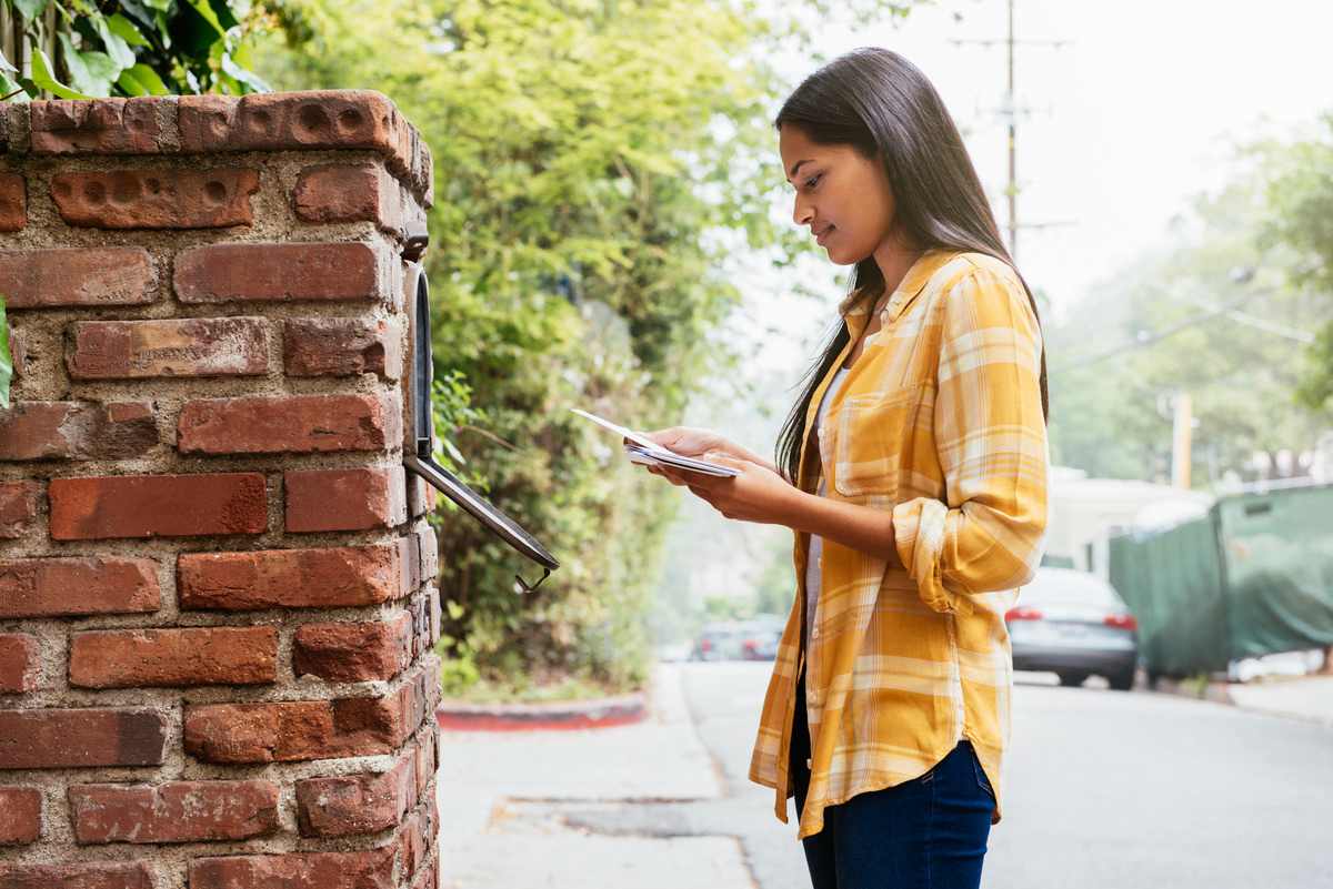 A woman retrieving her mail from her driveway mailbox.