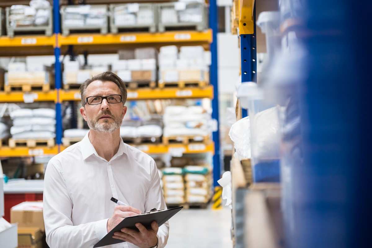 A man taking note on his clipboard in a warehouse.